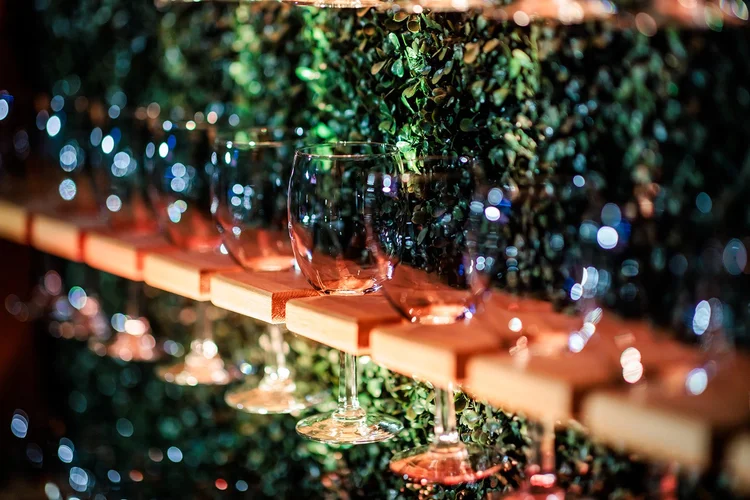 Wine glasses on lit wooden bar shelves with greenery backdrop corporate event Denver Colorado