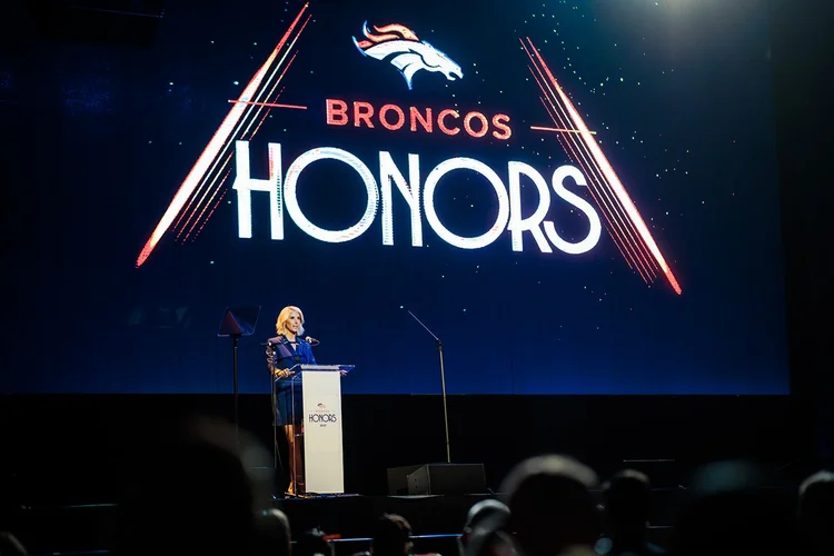 Host speaking at podium under Broncos Honors screen Mission Ballroom Denver event photography