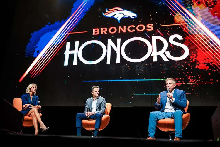 Panel discussion on stage at Broncos Honors Awards with three people in conversation chairs Mission Ballroom
