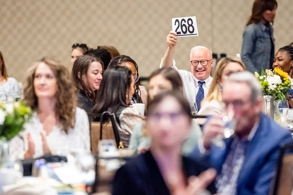 Attendee holding up paddle number 268 laughing at CCA Annual Luncheon fundraiser Hyatt Regency Aurora Colorado