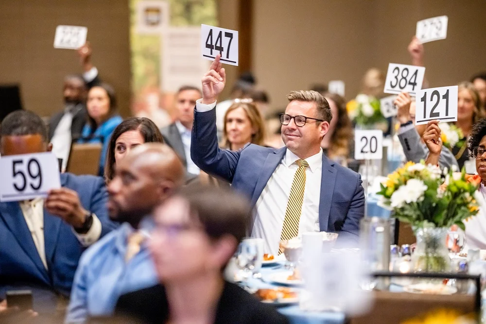 Multiple donation paddles raised across the room during paddle raise at Community College of Aurora Annual Luncheon