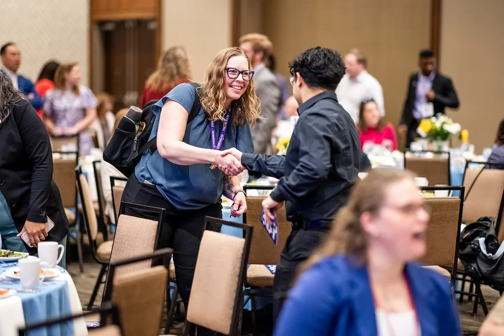Woman shaking hands and laughing while networking at Community College of Aurora fundraising luncheon Denver Colorado