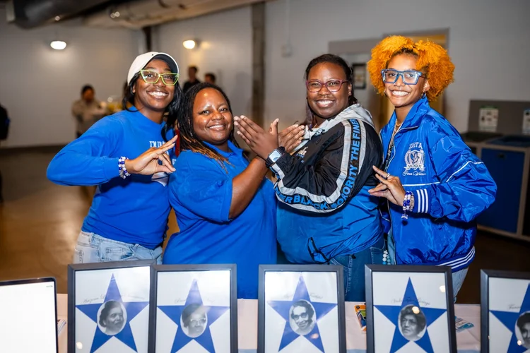 Zeta Phi Beta sorority members posing with framed portraits at Meet the Greeks MSU Denver