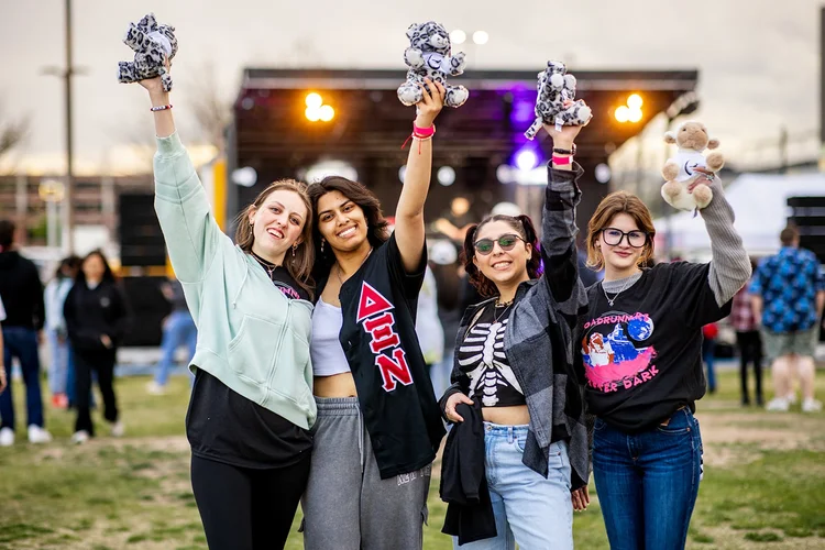 Four MSU Denver students holding stuffed animals in front of stage at Roadrunners After Dark