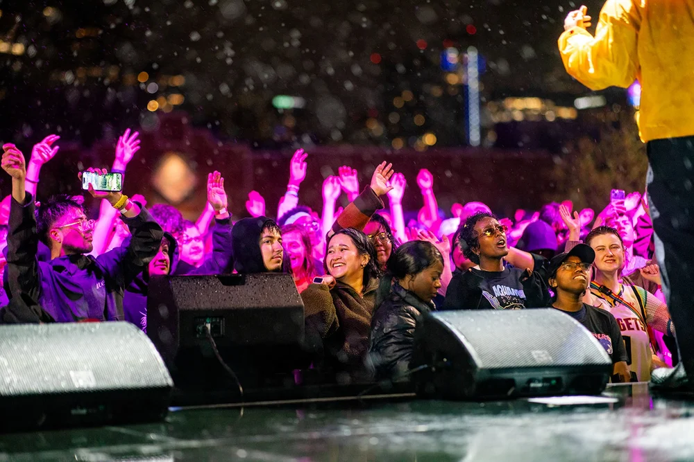 Front row crowd in pink light with hands raised at Roadrunners After Dark MSU Denver concert