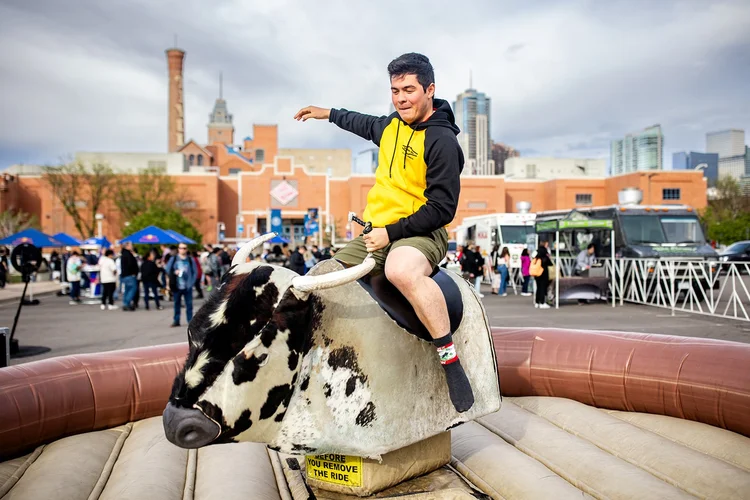 Student riding mechanical bull with Denver skyline behind at Roadrunners After Dark MSU Denver